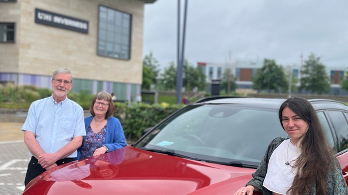 Three people standing by a red car,