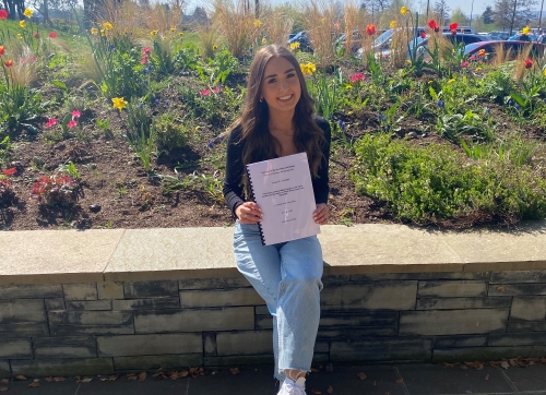 Lauren Geddes sitting on a wall with her completed dissertation