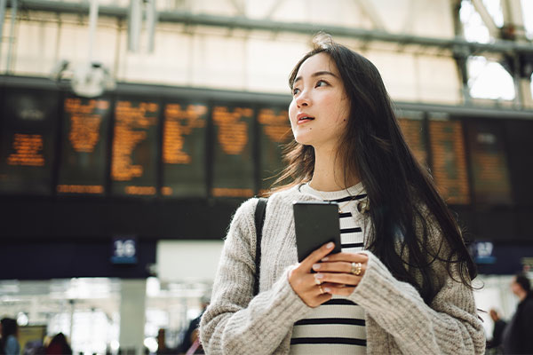 Young aspirational student arriving at a train station, with arrivals and departures board in the background